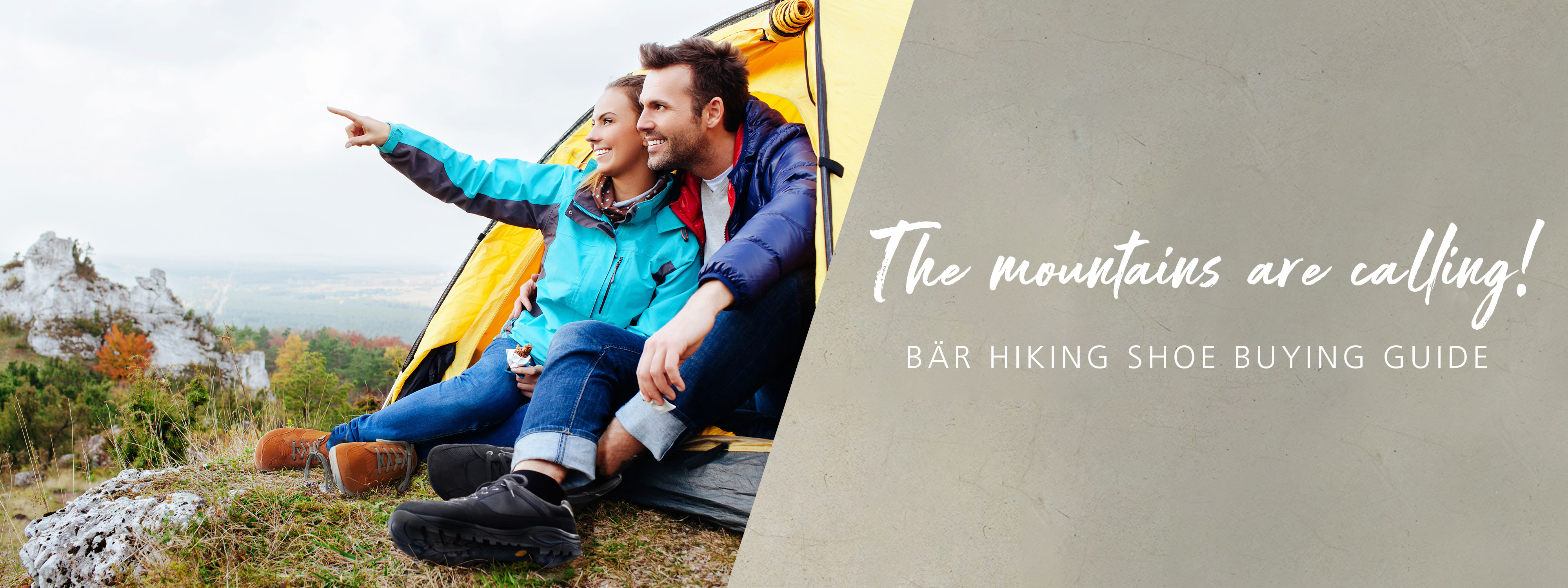 Couple Enjoying Mountain View Outside Tent - BÄR Hiking Shoe Buying Guide A happy couple sitting outside a yellow tent, pointing towards the mountains, with trees and rocky landscape in the background.