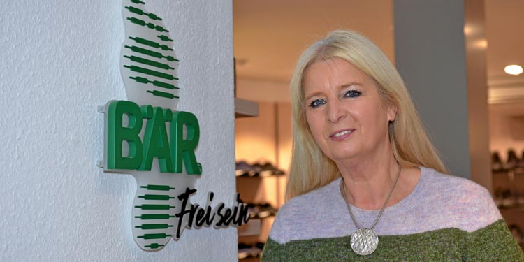 Dame vor BÄR-Schriftzug in einem Schuhgeschäft Blonde Frau steht lächelnd vor dem BÄR-Schriftzug in einem Schuhgeschäft