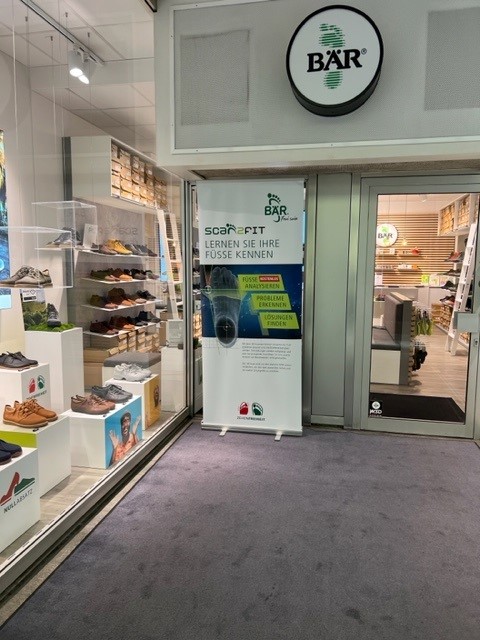 Schuhgeschäft mit modernem Fußanalysegerät Schuhgeschäft mit Schaufenster und einem modernen Fußanalysegerät, umgeben von einer Auswahl an Schuhen.