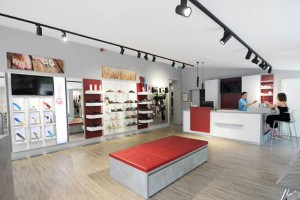 Innenansicht eines modernen Schuhladens mit elegantem Design, beleuchteten Regalen voller Schuhe und einem Verkaufsbereich mit zwei Personen.